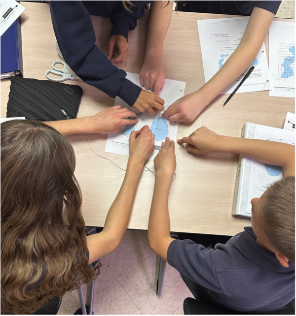 four sets of arms reach to center of table to work on a problem together.